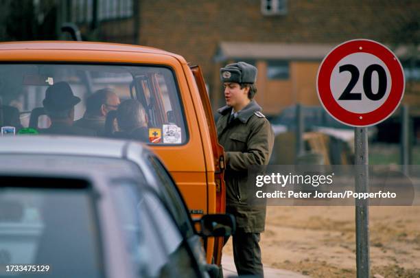 West German border guard checks the identity papers of citizens wishing to cross the border, known as the Iron Curtain, between West and East Germany...