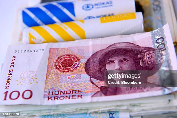 Bundles of mixed denomination Norwegian krone currency notes and coins sit in this arranged photograph in Oslo, Norway, on Friday, July 13, 2013....