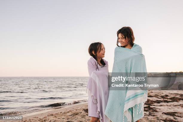 two sisters with bath towels on a beach looking at each other. - wrapped in a towel stock pictures, royalty-free photos & images