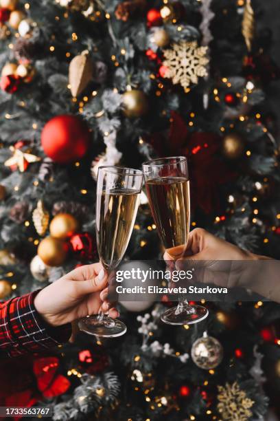 two people drink champagne and clink glasses against the background of a decorated christmas tree celebrate the new year holiday. christmas background - beauty care stock pictures, royalty-free photos & images