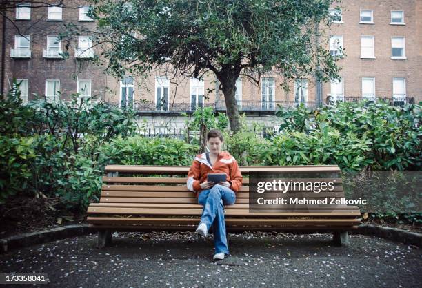 woman reading from her tablet in park - park bench fotografías e imágenes de stock