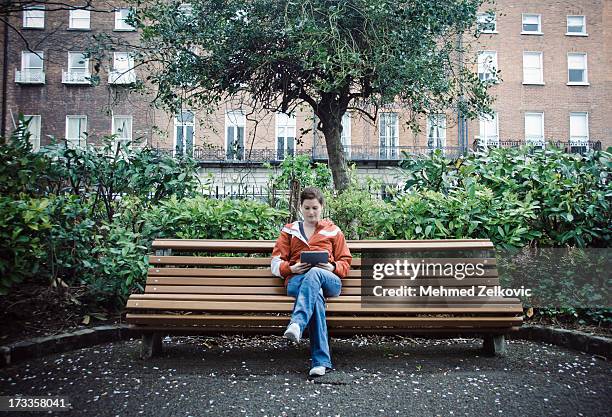 woman reading from her tablet in park - public park bench stock pictures, royalty-free photos & images