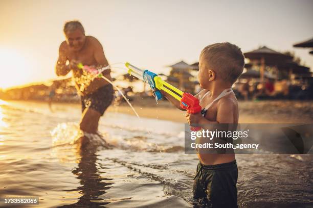 man and grandson playing with squirt guns - waterpistool stockfoto's en -beelden