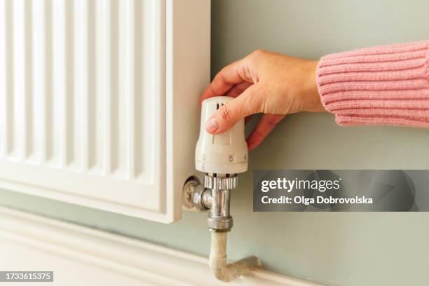 a female hand changing a temperature on a heating radiator at home - aardgas stockfoto's en -beelden