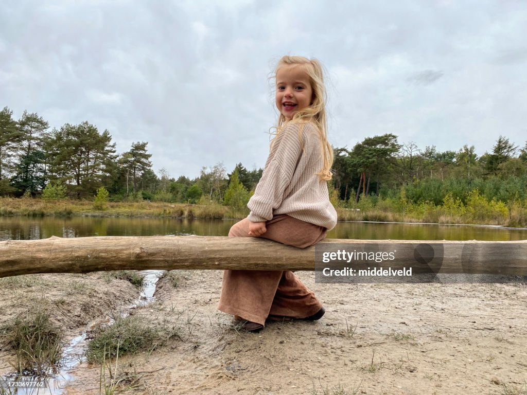 Fille en bas âge assise sur un tronc près de l’eau