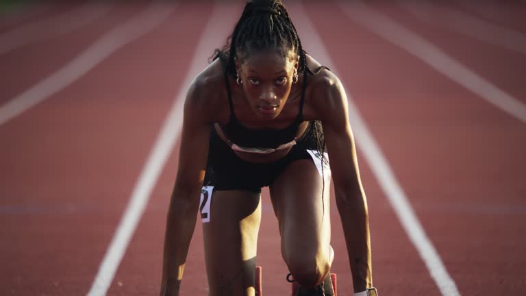 About 1 dramatic slow motion shot of female athlete getting on starting block to begin track race