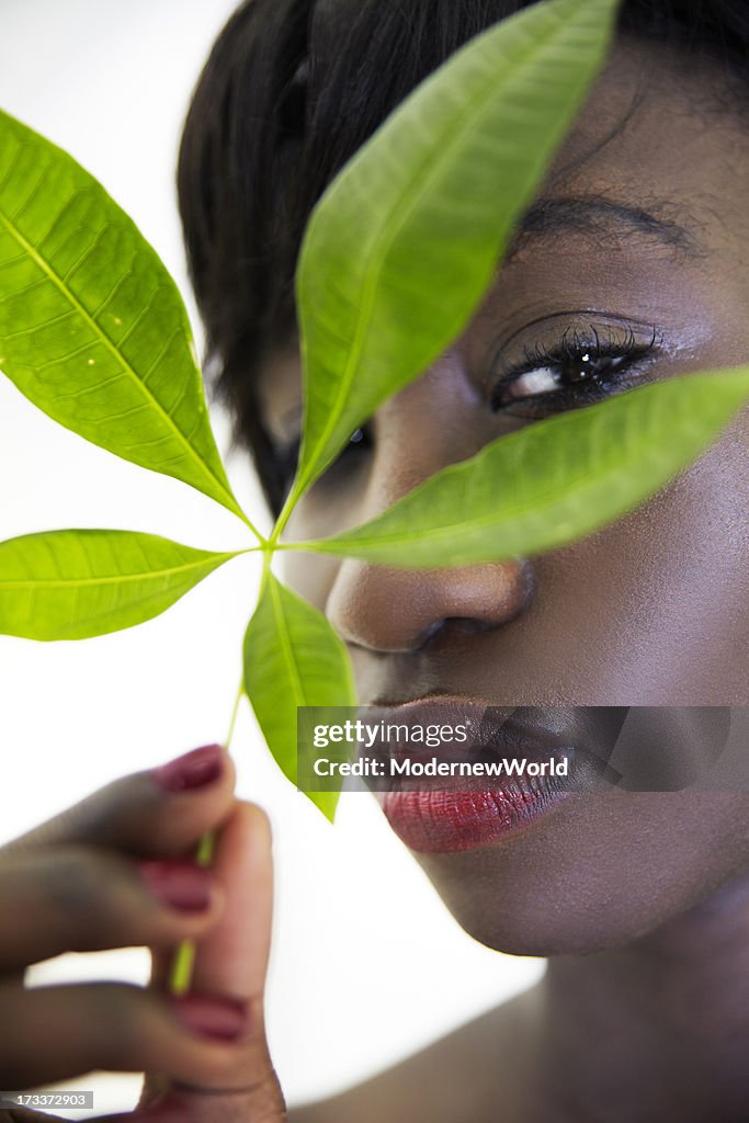 Black woman looking through green leaf