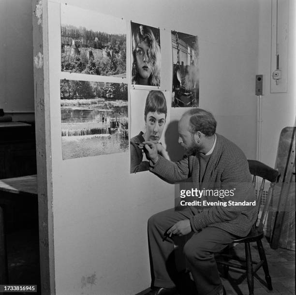 Photographer and artist Norman Tudgay touches up one of a series of photographs pinned to a wall, April 16th 1958.