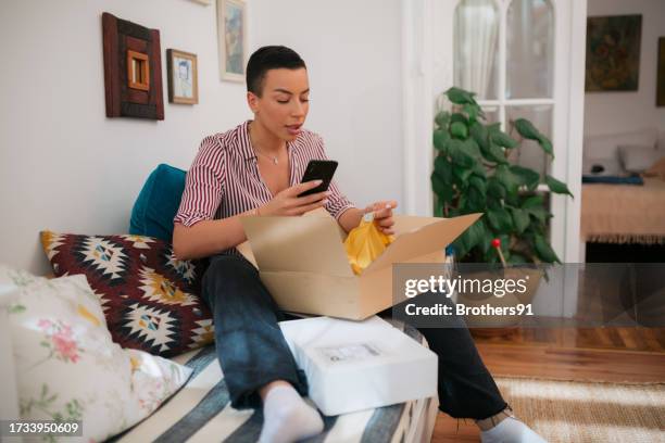 mujer joven tomando fotos de su ropa recién entregada usando su teléfono inteligente - devolución del saque fotografías e imágenes de stock