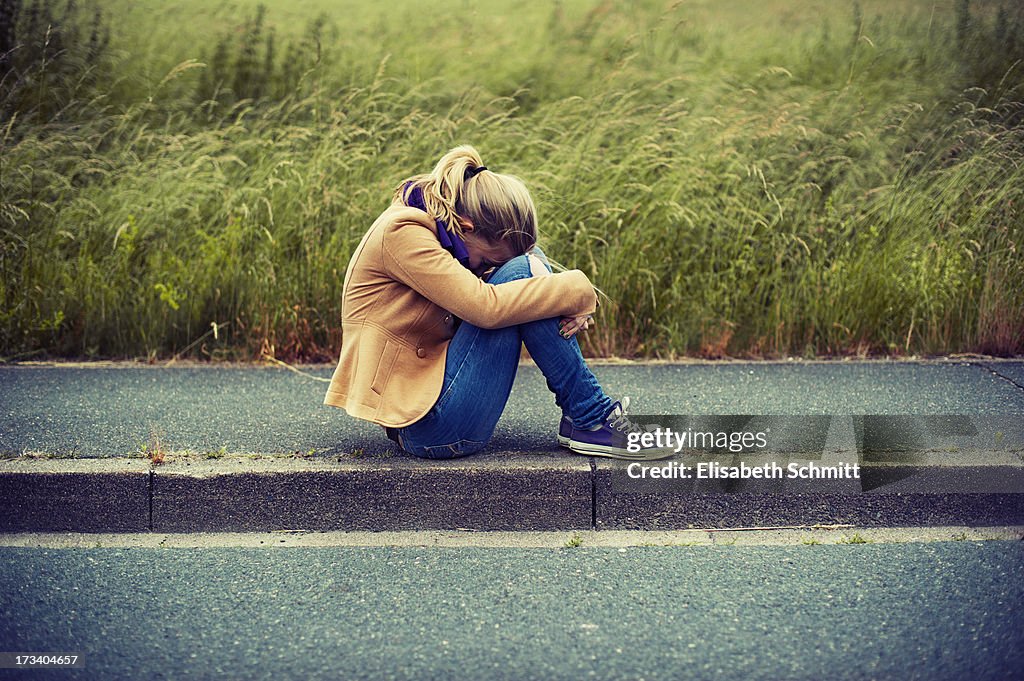 Girl sitting on sidewalk, hiding face