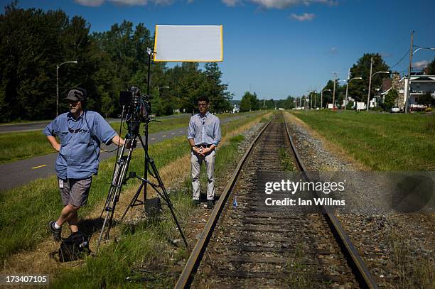 Members of the media stand next to train tracks July 13, 2013 in Lac-Megantic, Quebec, Canada. A train derailed and exploded into a massive fire that...