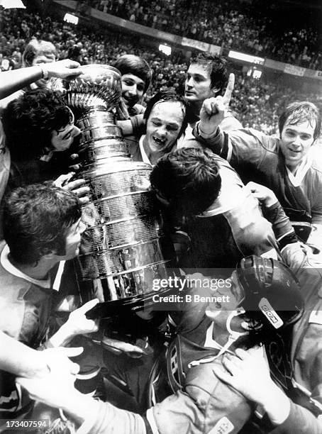 Yvan Cournoyer of the Montreal Canadiens, center, holds the Stanley Cup Trophy as he watches his teammates celebrate and kiss the trophy after they...