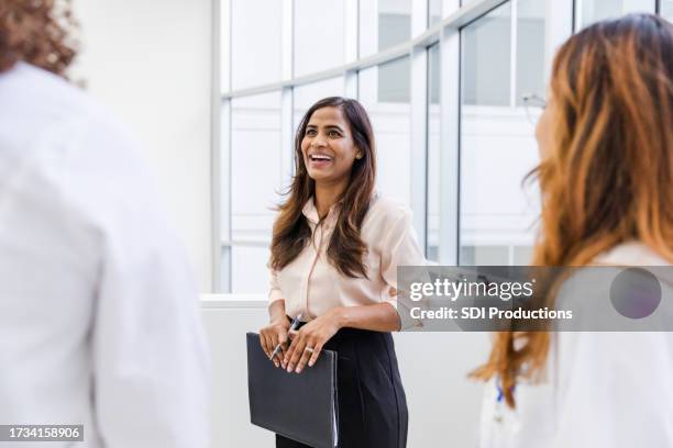 mid adult female social worker smiles while talking with her colleagues - mannerism stock pictures, royalty-free photos & images