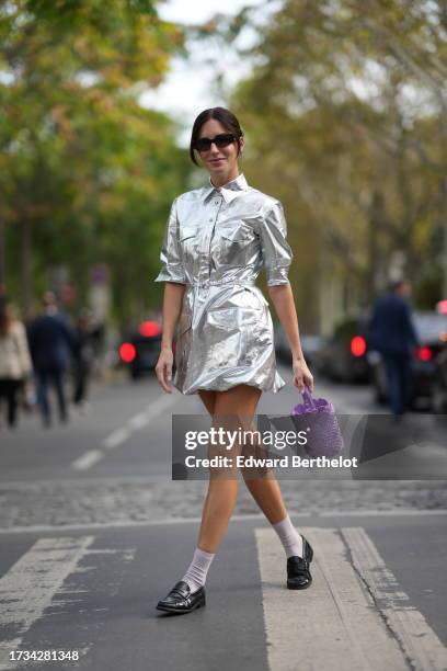 Gala Gonzalez wears sunglasses, a silver shiny shirt / dress, a purple bag, white socks, black leather loafers shoes, outside Rabanne, during the...