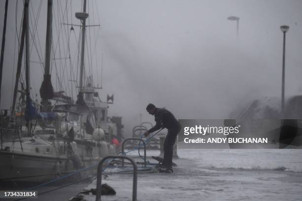 Boat owner braves the conditions inside the harbour to secure boats in Stonehaven on the east coast of Scotland on October 19 as wind and rain from...