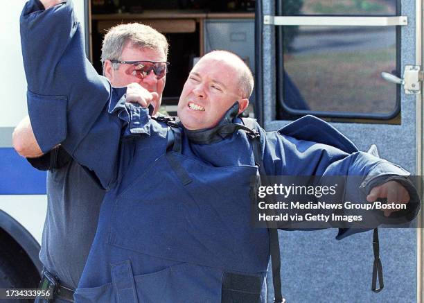 Officer Edward O'Toole assists Michael Kane into a bomb suit at the scene of a suspicious package in West Roxbury. STAFF PHOTO BY JON HILL saved in...