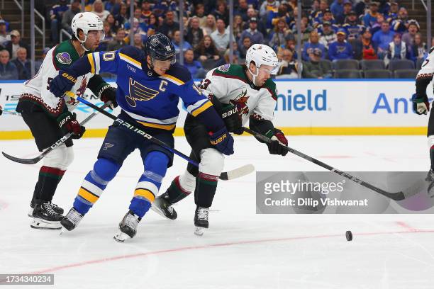 Brayden Schenn of the St. Louis Blues fights Sean Durzi and Michael Carcone of the Arizona Coyotes for control of the puck during the first period at...