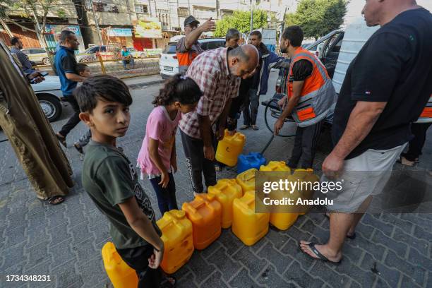 Officers fill the plastic bottles of citizens waiting to get clean water from the mobile water tanks as the Israeli attacks continue in Rafah, where...