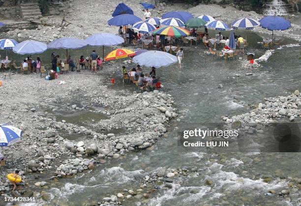 Tourists sitting under the umbrellas, enjoy their light hours at a waterside teahouse at a tourist attraction in Dujiangyan city, about 60 kilometers...