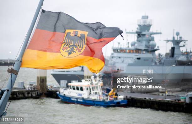 October 2023, Lower Saxony, Wilhelmshaven: A flag of the Federal Republic of Germany flies in the strong wind aboard the frigate "Baden-Württemberg"...