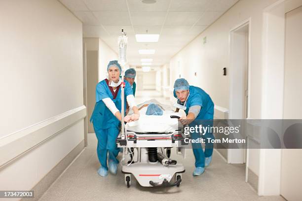 doctors pushing patient on gurney down hospital corridor - pushing stretcher stock pictures, royalty-free photos & images