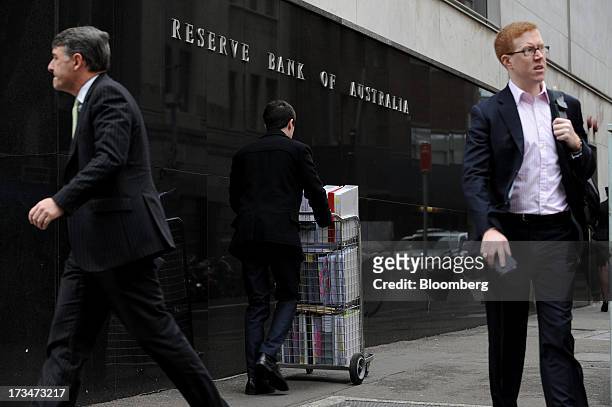 Pedestrians and a man pushing a cart of papers walk past the Reserve Bank of Australia headquarters in the central business district of Sydney,...