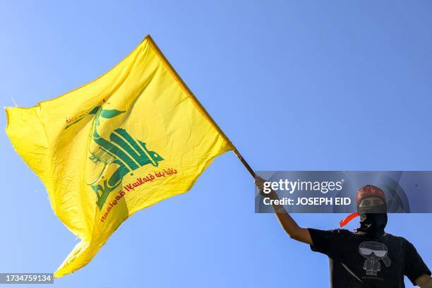 Masked demonstrator waves a flag of the Lebanese Shiite movement Hezbollah during a demonstration supporting the Palestinians in Beirut on October 20...