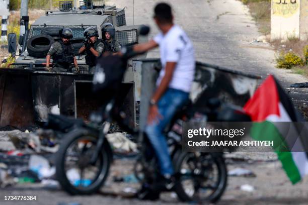Man carries a Palestinian national back on a motorcycle as he faces Israeli troops during clashes with them at the northern entrance of the West Bank...