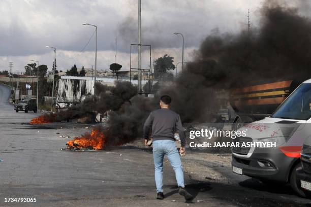 Man walks near burning tyres during clashes between Palestinians and Israeli forces at the northern entrance of the West Bank city of Ramallah near...