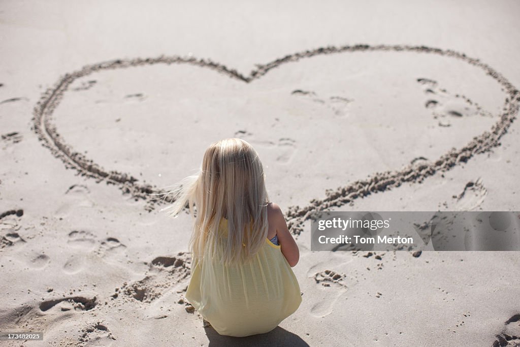 Girl drawing heart in sand on beach