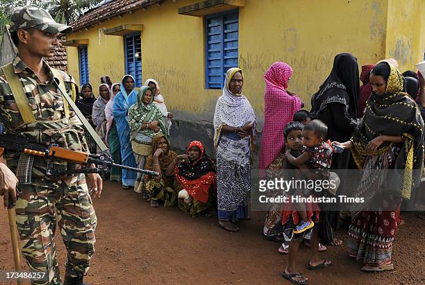 Security personel stand on gaurd as women are standing in line at polling booth to vote during second phase of West Bengal panchayat elections on...