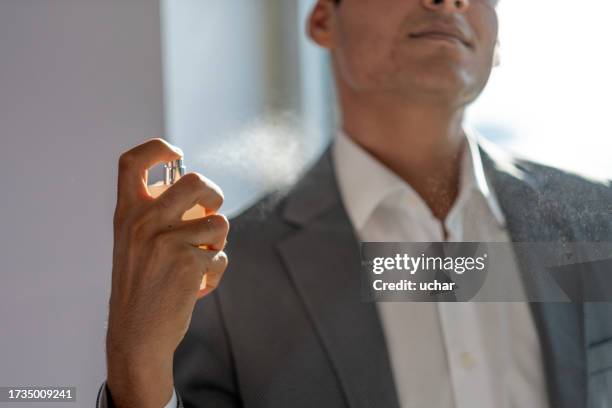 young man sprays perfume on his body on his way to work in the morning - perfumado imagens e fotografias de stock
