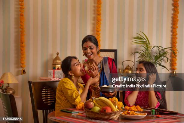 mother feeding rasgulla to her daughter while sitting together in the dining room - bengali girl stock-fotos und bilder