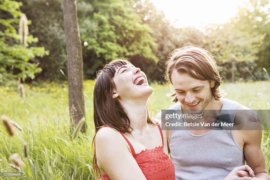 Couple laughing, sitting outdoors in grass.