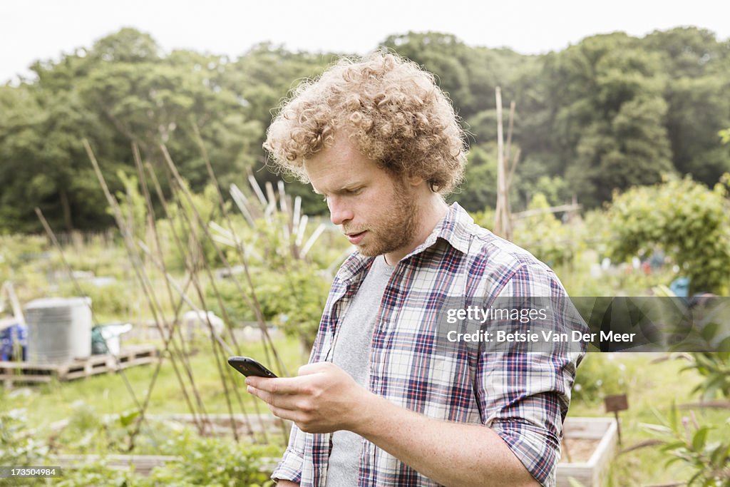 Man checking phone, standing in allotment.