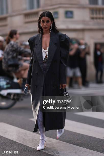 Anaa Saber is seen wearing an oversized coat with shoulder pads, pinstripes in dark grey, a shoulderless top in white and with a bow, along with a...