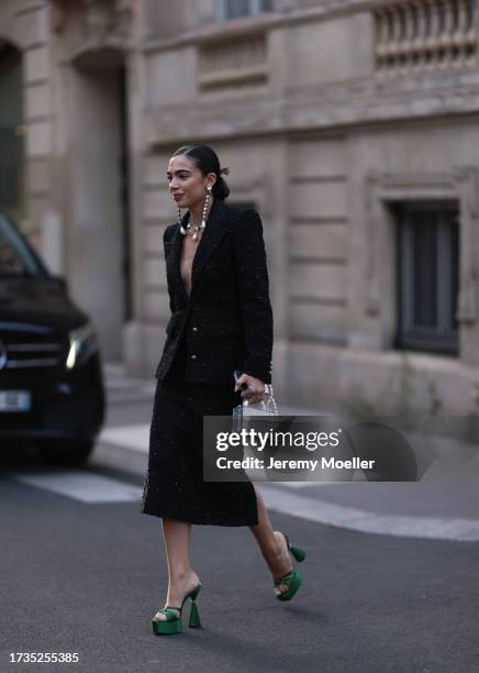 Fashion Week Guest is seen wearing a black blazer with shoulder pads, gold buttons and silver details, a black midi skirt, green high heels with...