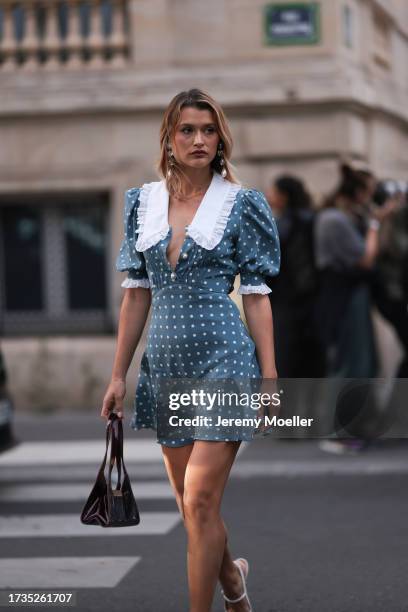 Chloe Lecareux is seen wearing a blue satin dress with padded shoulder sleeves, white collar, black patent handbag, white high heels and long pearl...