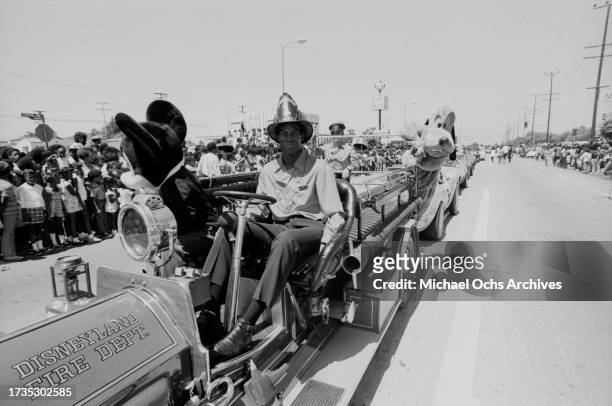 Participants wearing Mickey Mouse and Pluto costumes alongside firefighters riding the Disneyland Fire Dept fire engine during the 1972 Watts Summer...