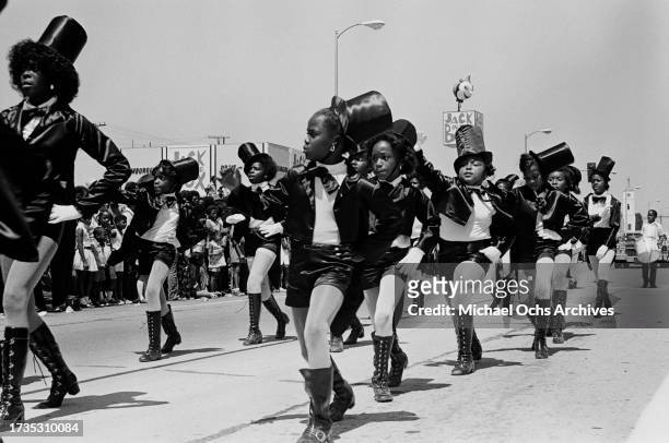 Young girls, wearing matching outfits comprising black top hats and black jackets, black skirts and black boots, march in unison during the 1972...