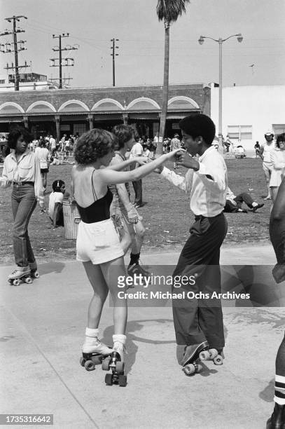 Two people on roller skates among other roller skaters on the beachfront of Venice Beach, in the Venice neighbourhood of Los Angeles, California,...