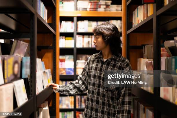 a young man picks out a book at a bookstore. - textbook stock pictures, royalty-free photos & images