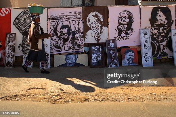 Woman walks past artwork of Nelson Mandela and other freedom icons by street artist Xolani Mahlangu in Soweto Township on July 16, 2013 in Soweto,...