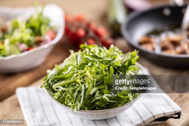 frisee salad in a bowl on the kitchen table. bowls of mixed vegetables are prepared behind him. - endivie stock-fotos und bilder
