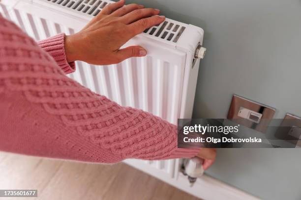 woman's hands adjusting a heating temperature on a radiator at home - heizung stock-fotos und bilder