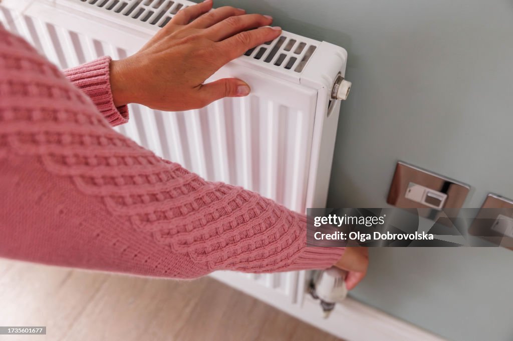 Woman's hands adjusting a heating temperature on a radiator at home