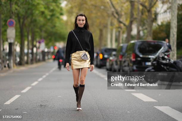 Mary Leest wears a black shirt, a silver metallic bag from Rabanne, a golden mini skirt, knee high tights, golden shoes, outside Rabanne, during the...