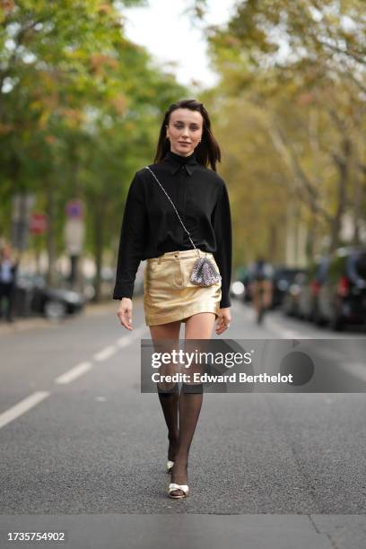 Mary Leest wears a black shirt, a silver metallic bag from Rabanne, a golden mini skirt, knee high tights, golden shoes, outside Rabanne, during the...