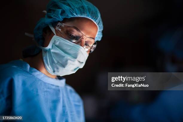 doctora hispana mirando hacia abajo hacia el paciente en la sala de operaciones de cirugía médica en el hospital - cirugia fotografías e imágenes de stock