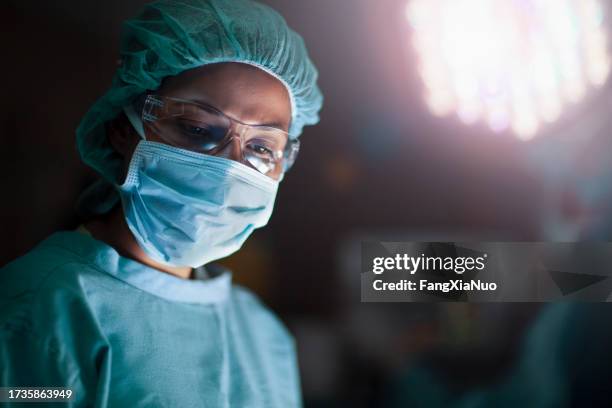 hispanic woman doctor looking down towards patient in medical surgery operation room in hospital with light - cirurgião imagens e fotografias de stock
